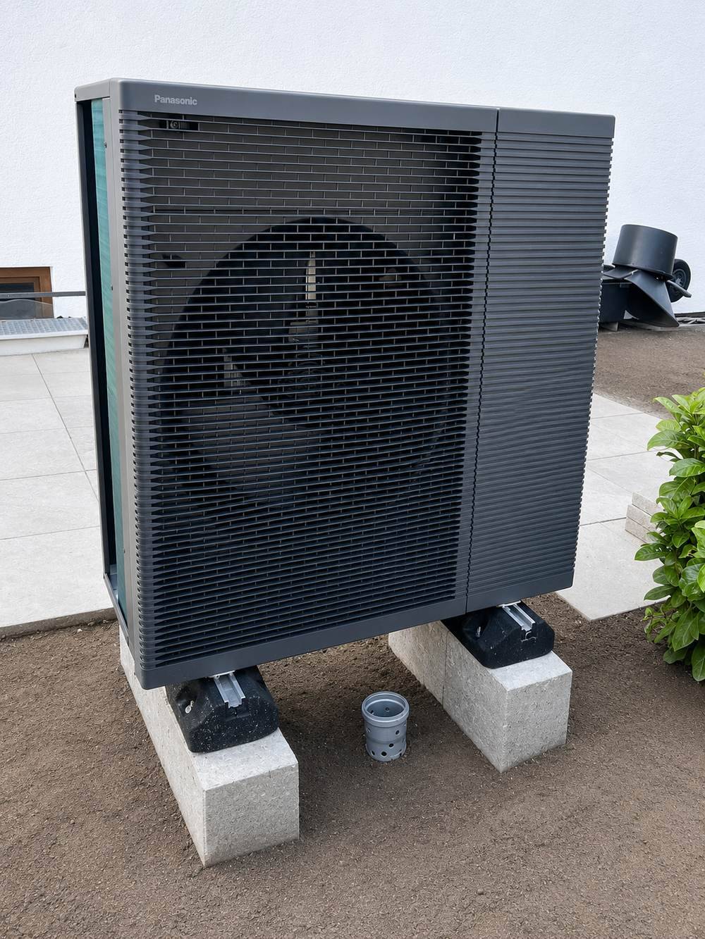 Außeneinheit der Wärmepumpe auf Betonsockeln neben der Terrasse